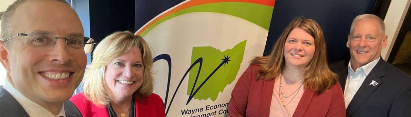 Four professionals smiling together in front of the Wayne Economic Development Council banner.