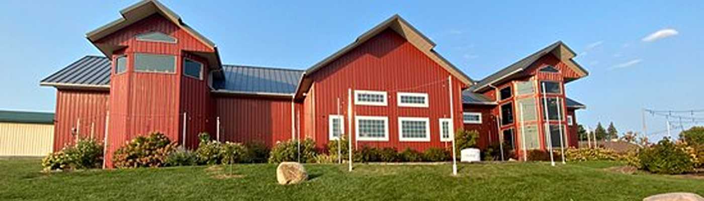 Red metal barn-style commercial building exterior on a grassy lot.