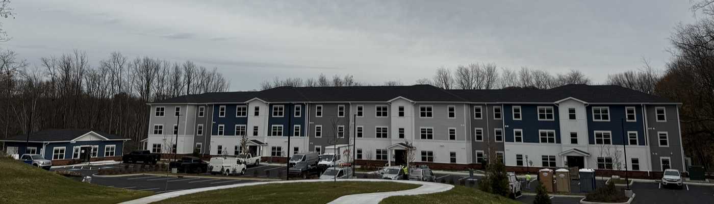 Newly constructed multi-story apartment complex with parking area and surrounding trees.