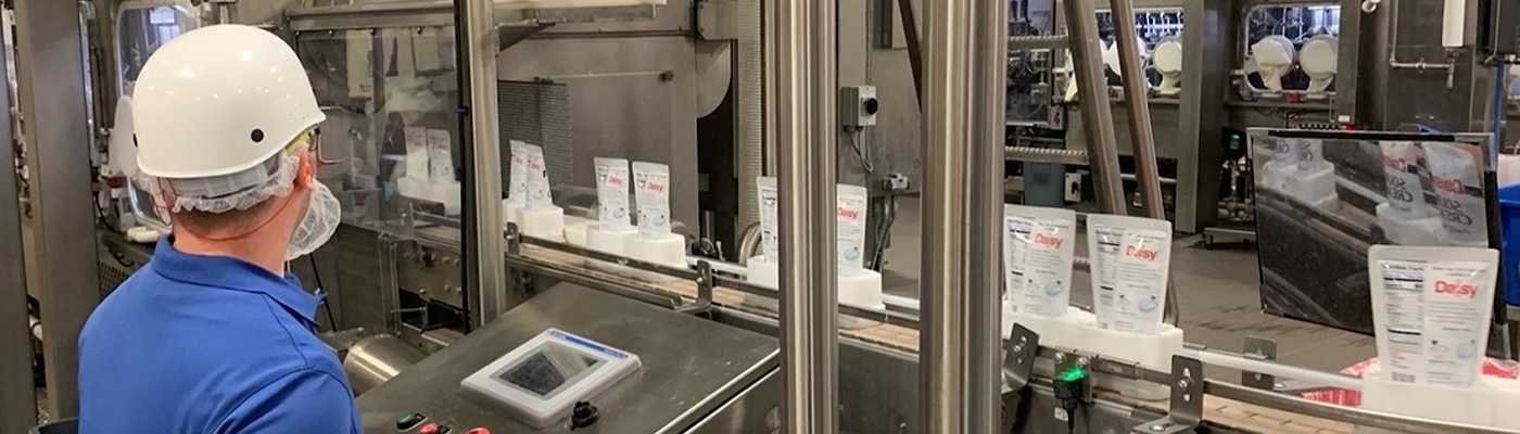 Worker monitoring automated packaging line in a manufacturing plant.